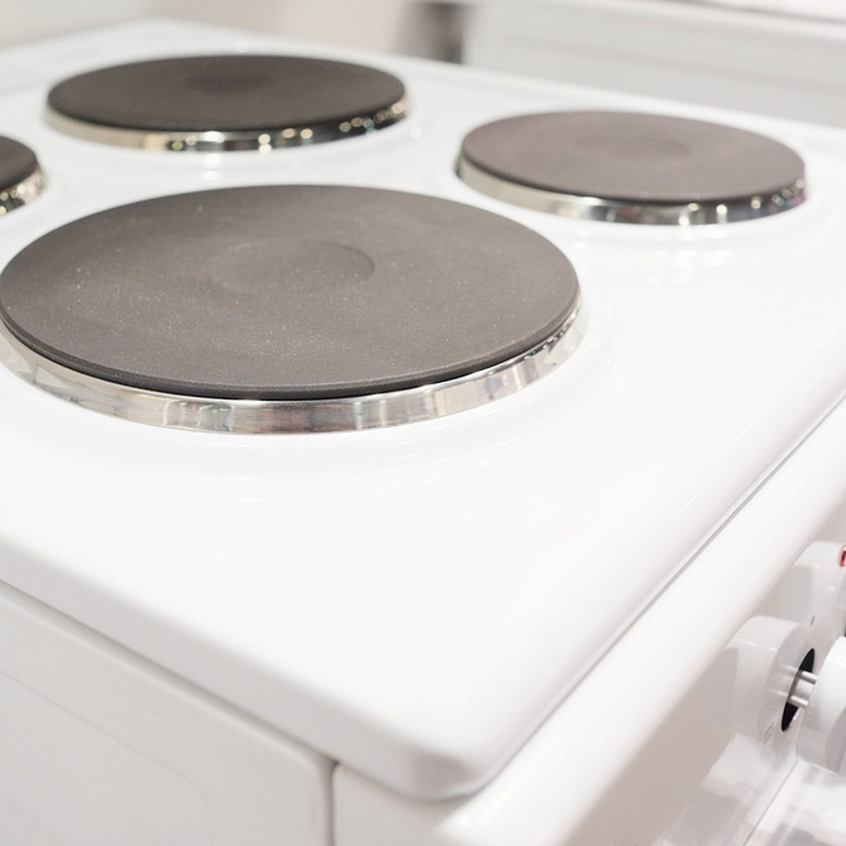 A white stovetop with four black burners rests on a kitchen counter, showcasing polished metal rims around each burner in a clean, modern en