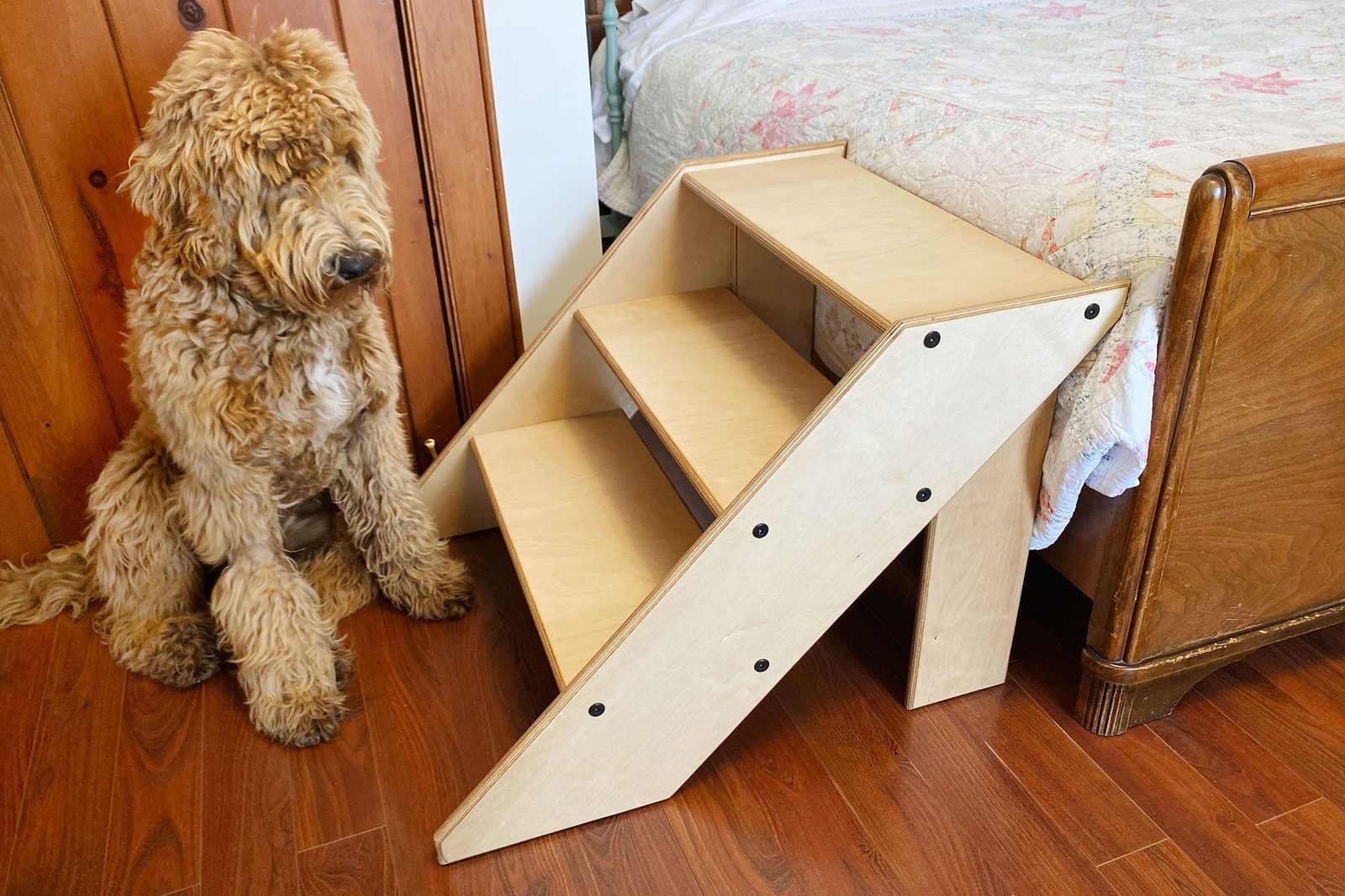 A wooden dog ramp stands next to a sleeping dog, providing access to a bed in a cozy bedroom with wooden walls and flooring.