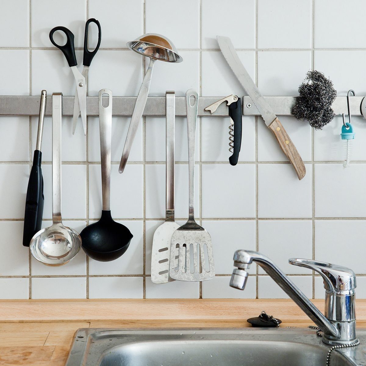 Kitchen stuff on magnet line against wall tiles.