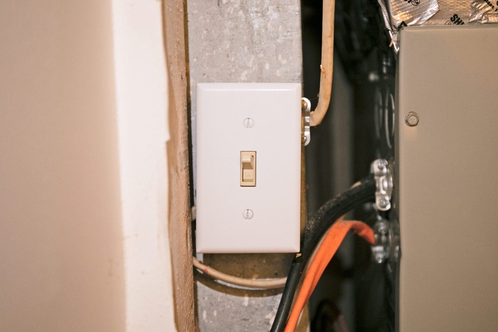 A light switch mounted on a wall activates and deactivates lighting within an indoor utility space, surrounded by wires and metal structures