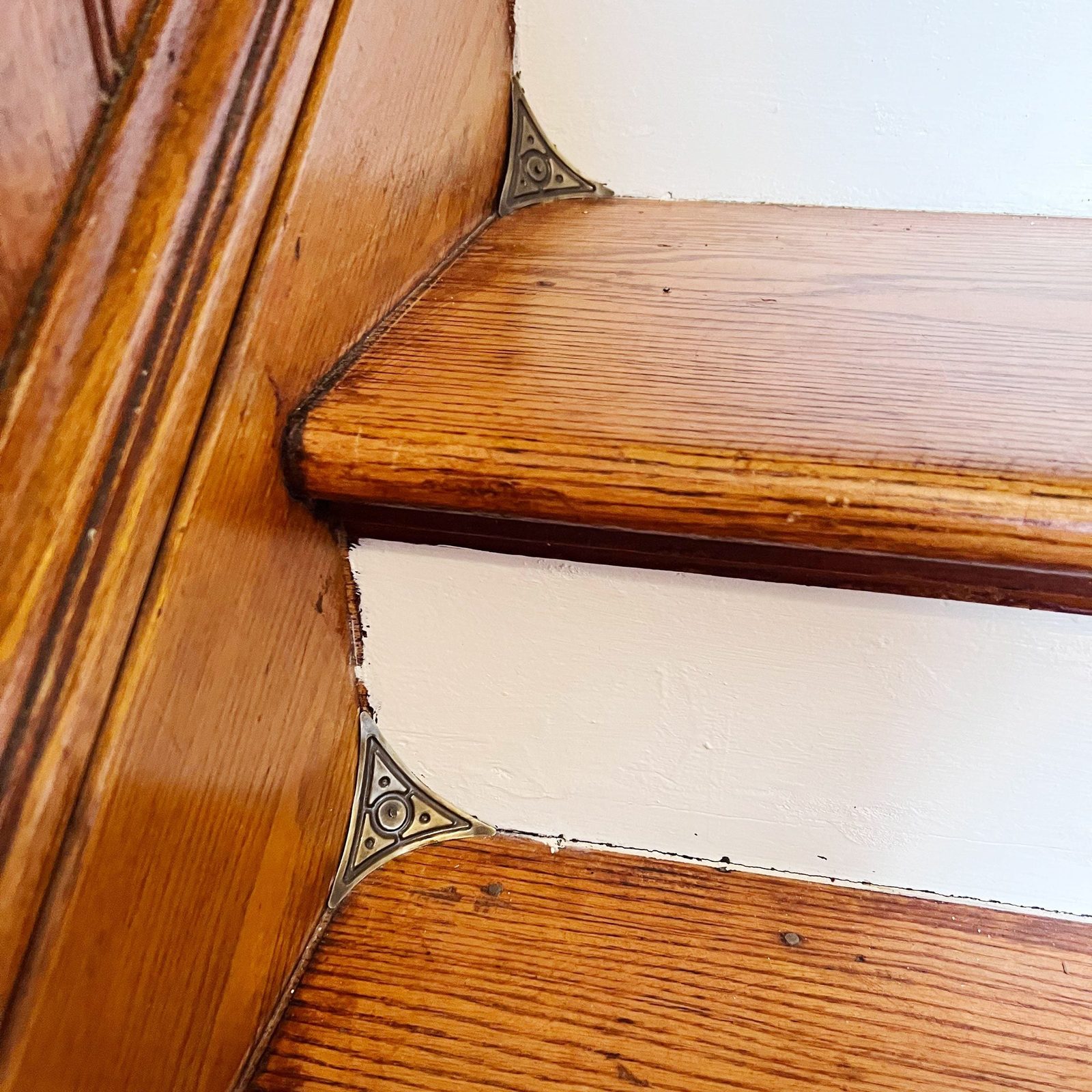 Wooden stair treads display decorative metal corner brackets, highlighting craftsmanship. The white wall provides a clean backdrop, accentua
