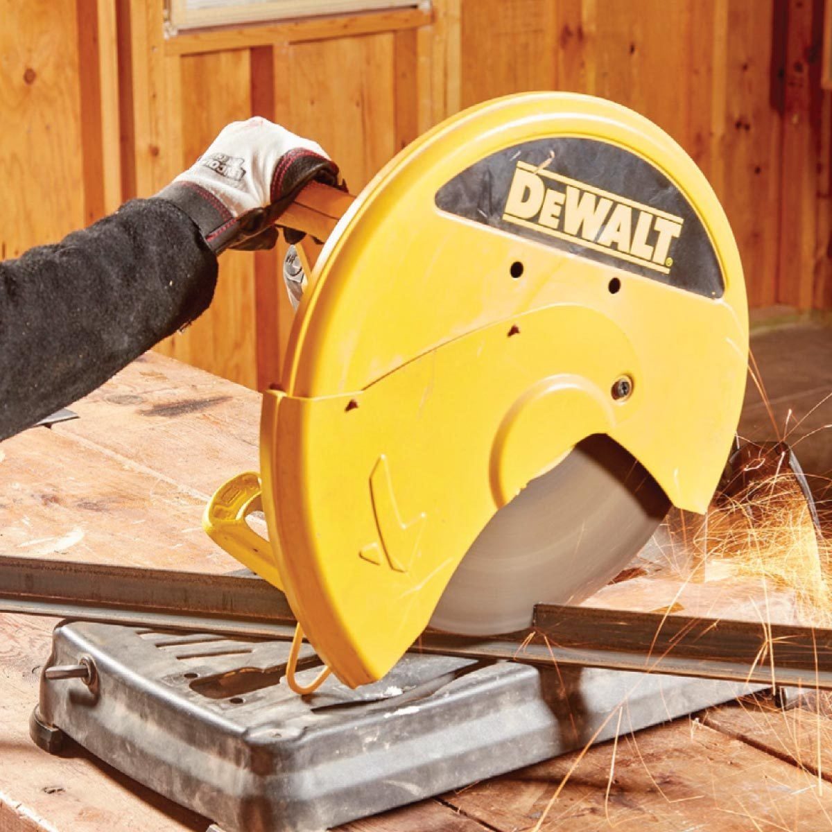 A yellow circular saw cuts through metal, emitting sparks, while a gloved hand holds the material steady on a wooden workbench in a wooden w