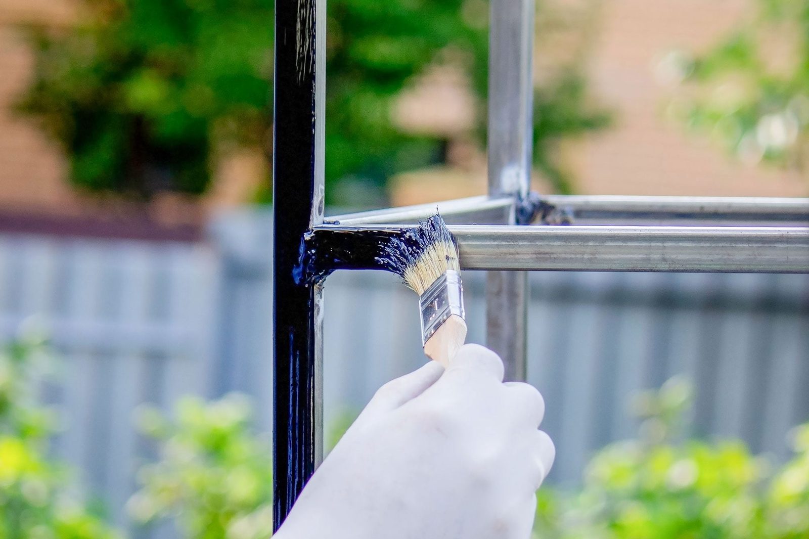 A Man Paints Metal With Black Paint With A Brush