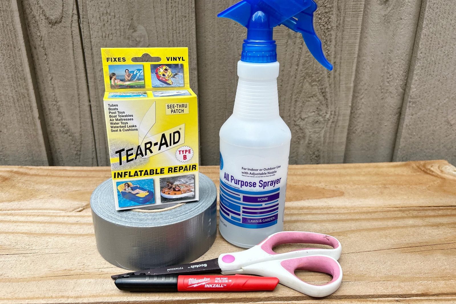 Tear-Aid repair kit and various tools rest on a wooden surface, preparing for repairing inflatables in an outdoor setting against a textured