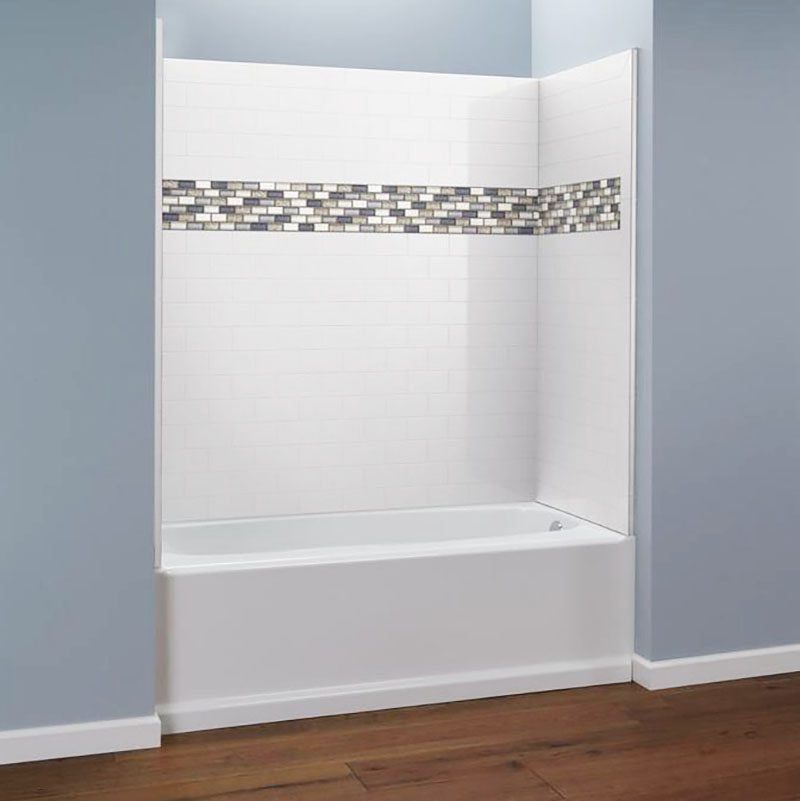 A bathtub is installed in a simple bathroom, surrounded by white tiled walls featuring a decorative mosaic strip, with blue-painted walls an