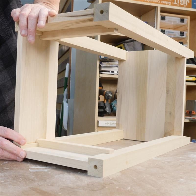Wooden frame is being assembled with hands, surrounded by tools and materials in a workshop setting.