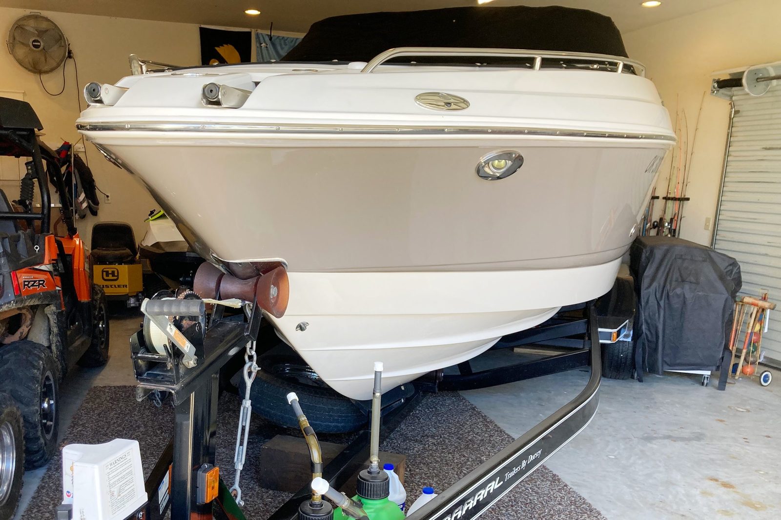 A boat is parked on a trailer inside a garage, surrounded by various equipment and clutter, including tools and an off-road vehicle.
