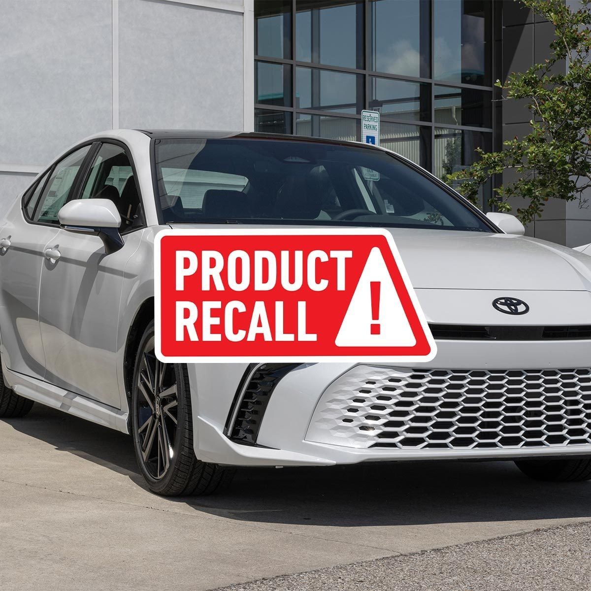 White toyota camry parked on asphalt with a red "product recall" sticker on top