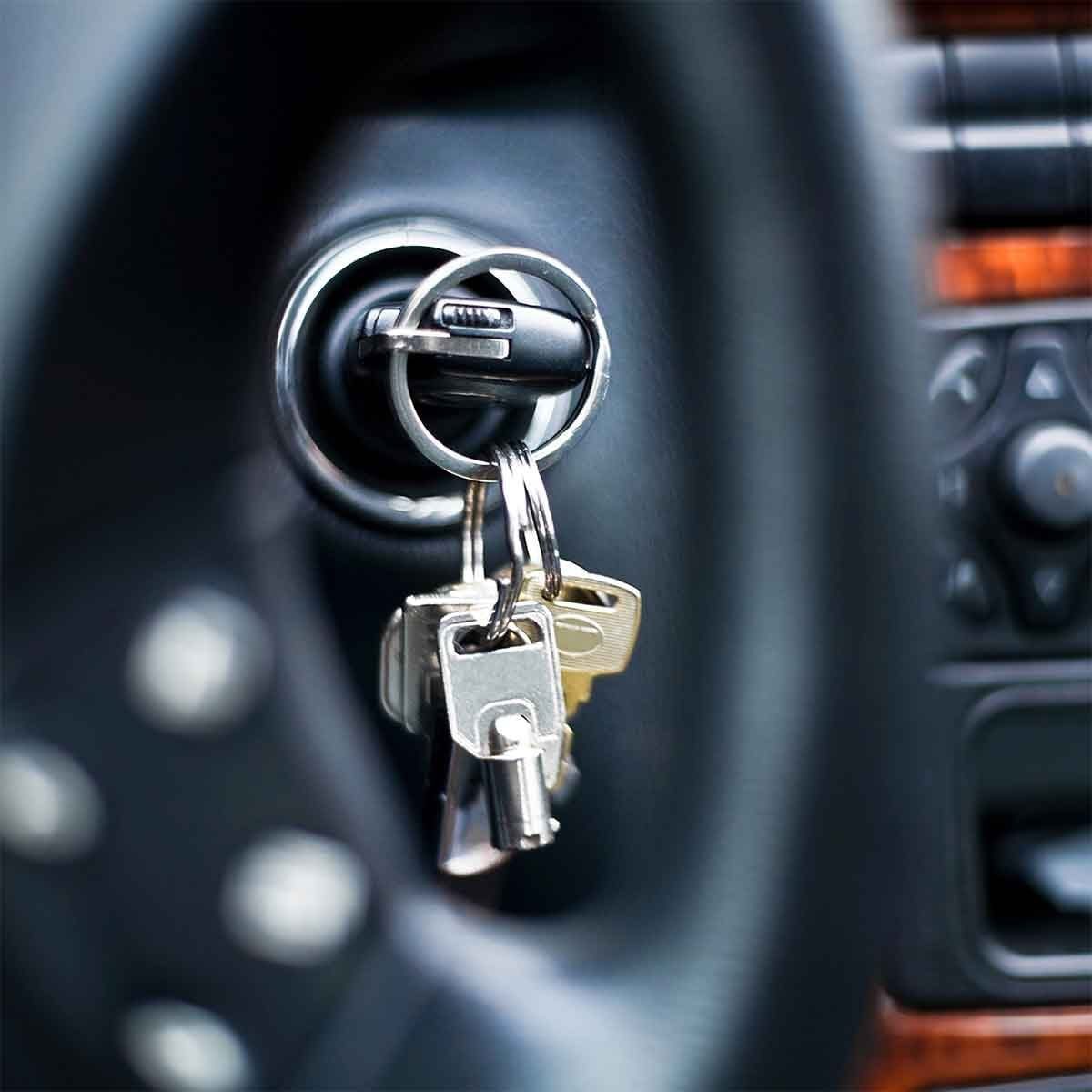 A car key is inserted in the ignition, ready to start the vehicle, surrounded by a steering wheel and dashboard controls.