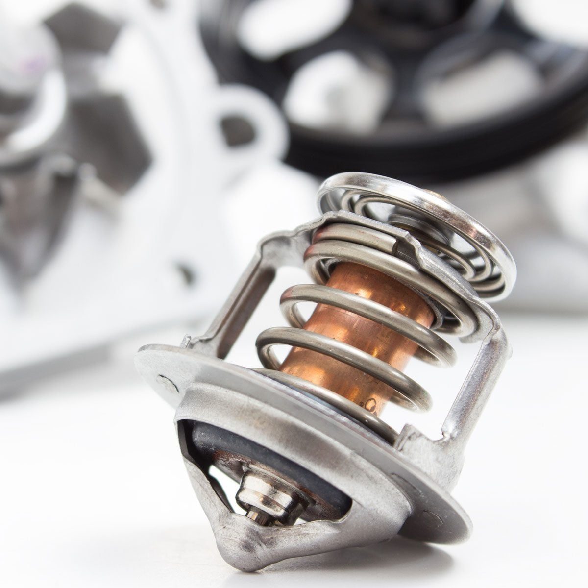 A metallic thermostat sits prominently with a copper insert and springs, placed against a blurred background of mechanical components in a w