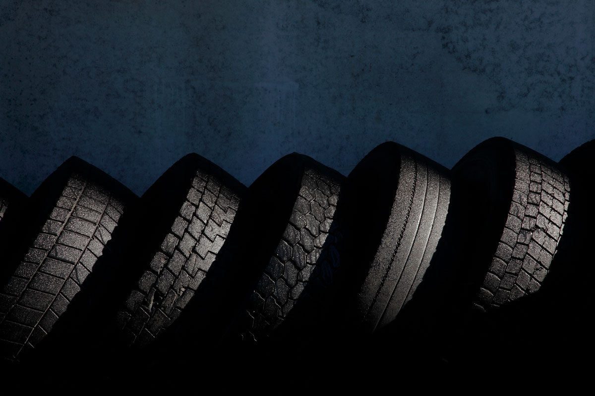 A series of six car tires are arranged in a curved line, showcasing varied tread patterns against a dark background, highlighting texture an