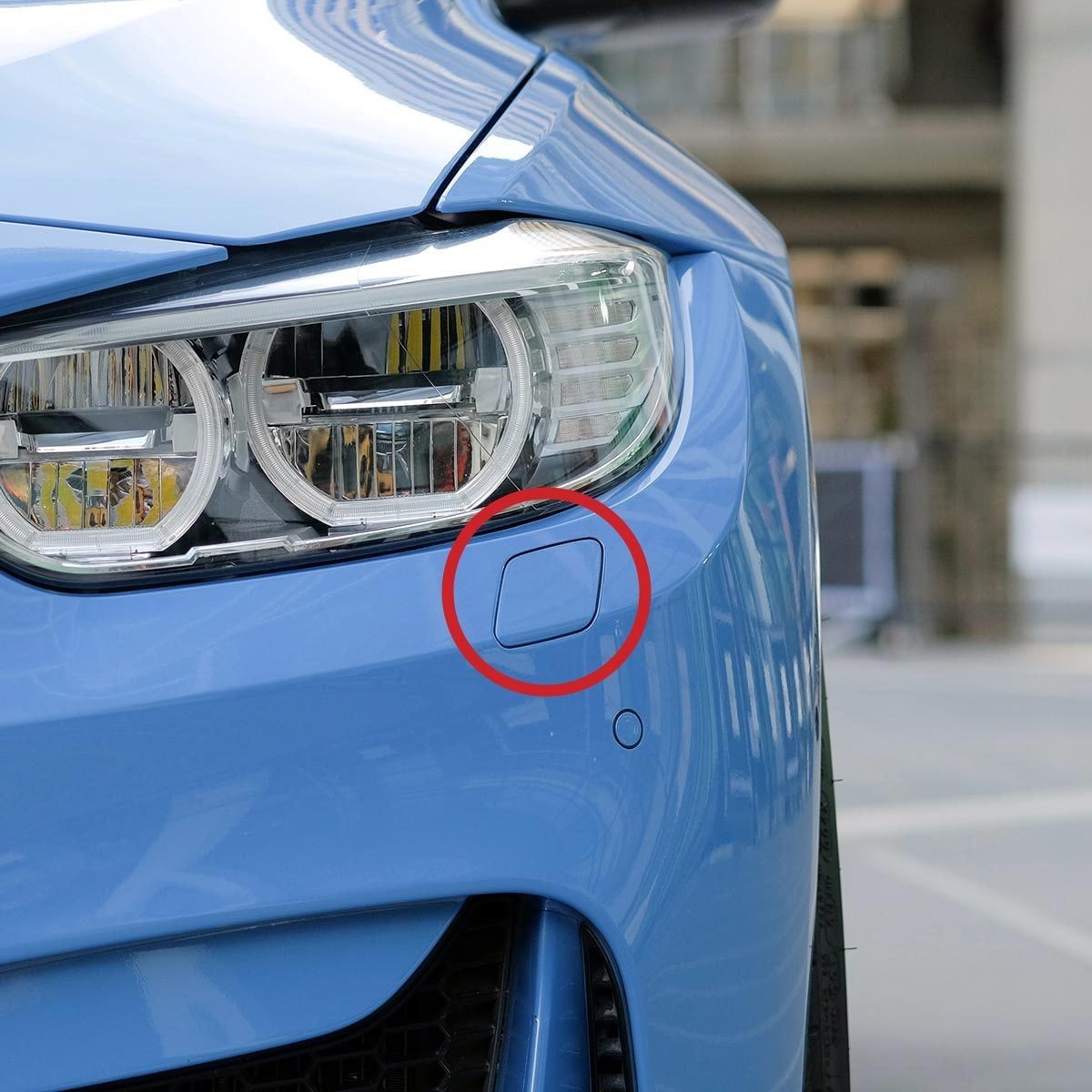 Close-up of the front bumper of a BMW M4 sport blue car, with a small, four-sided panel below the headlight circled in red