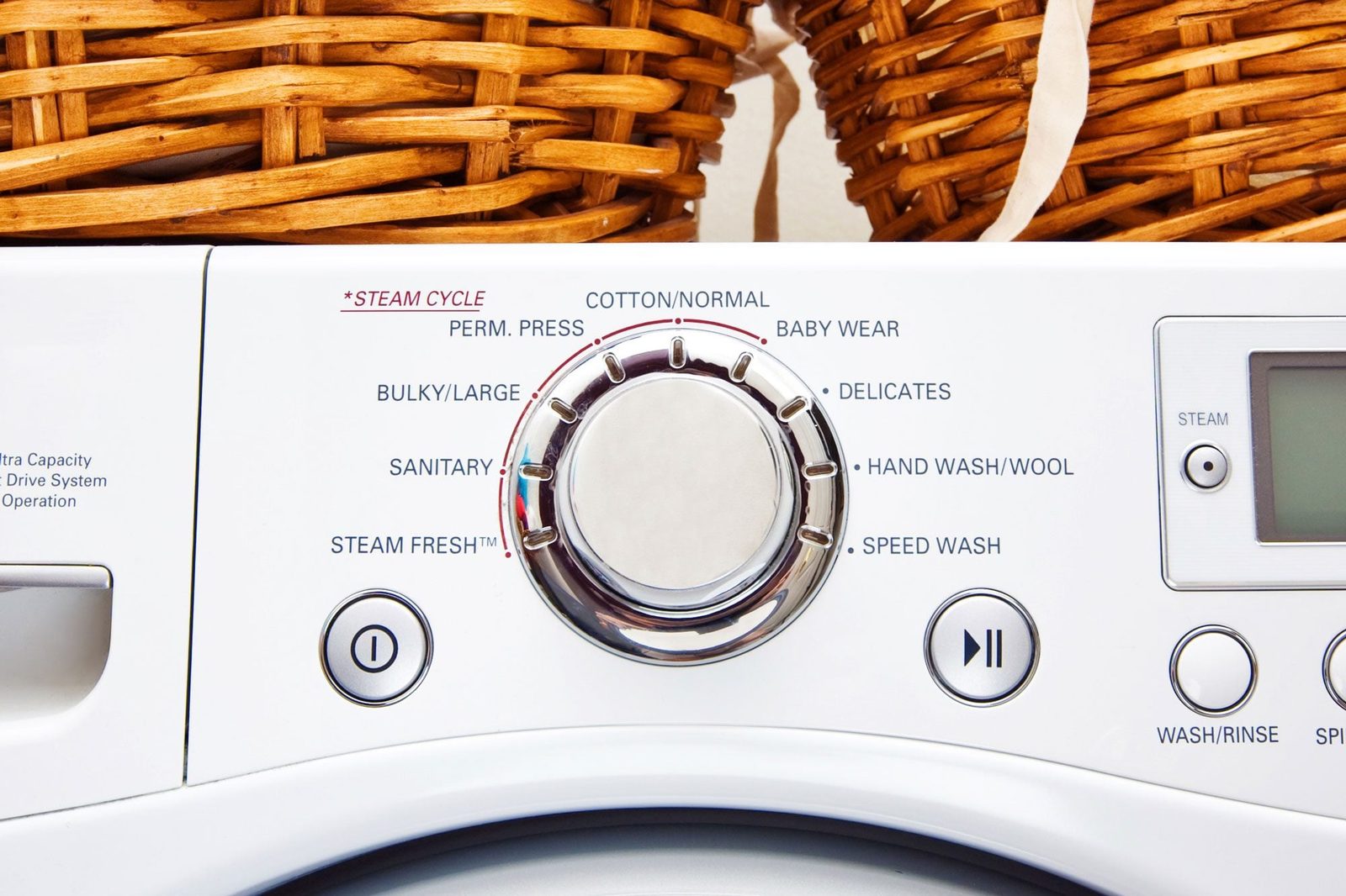 A washing machine's control panel displays various wash settings, including "STEAM CYCLE." Above, woven baskets provide storage for laundry