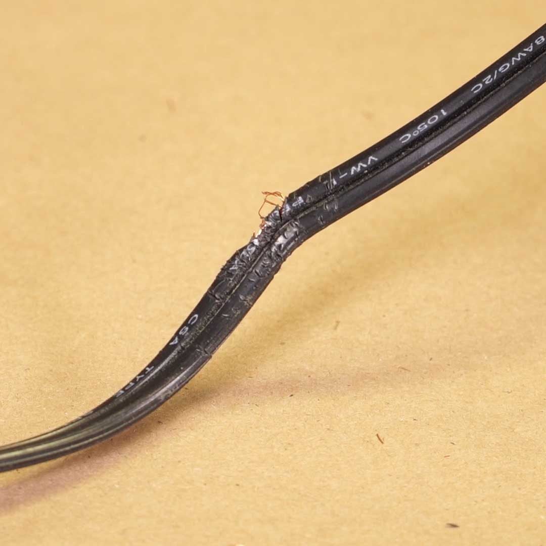 A damaged electrical wire lies on a brown surface, showing exposed copper and frayed insulation, indicating potential hazards in its usage.