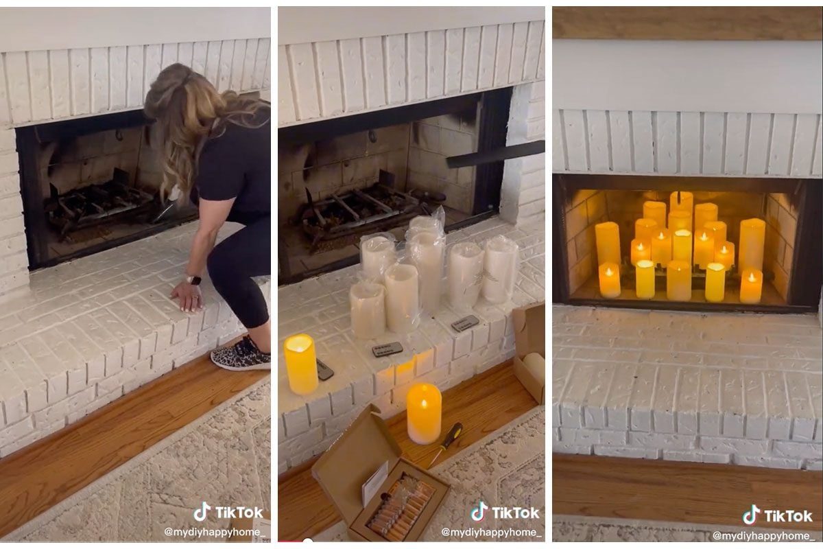 A person cleans a white brick fireplace, preparing it for decorative candles set on the hearth, illuminated with warm light in a cozy room.