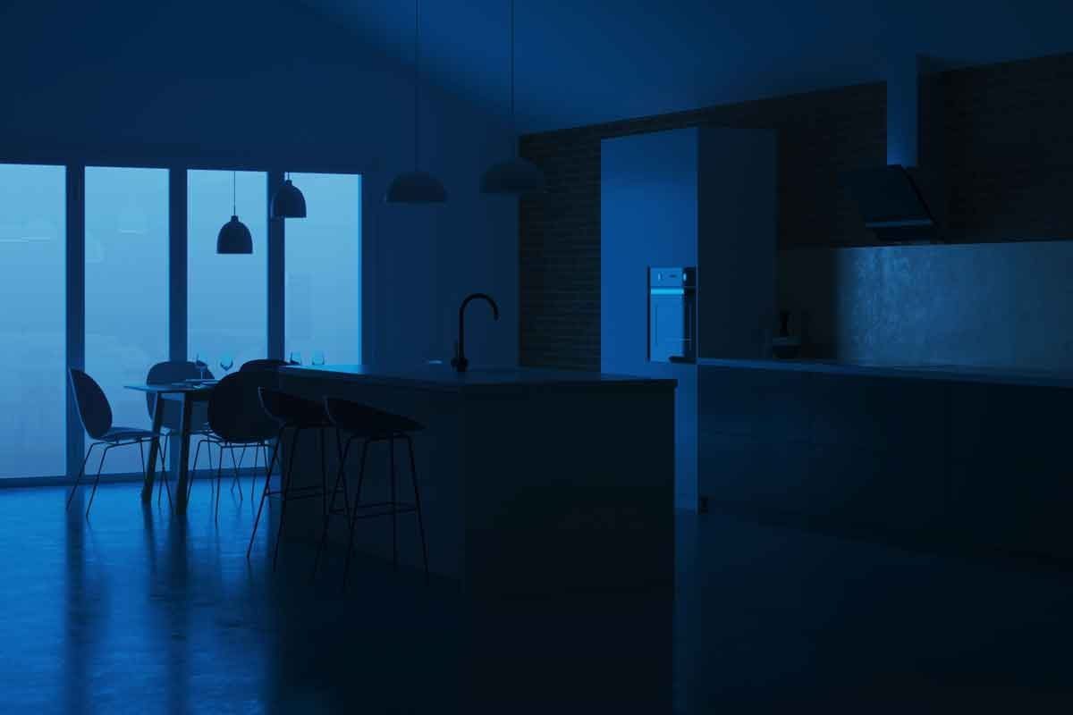 A modern kitchen features an island with tall stools, illuminated by pendant lights, in a dimly lit space with large windows revealing a mis