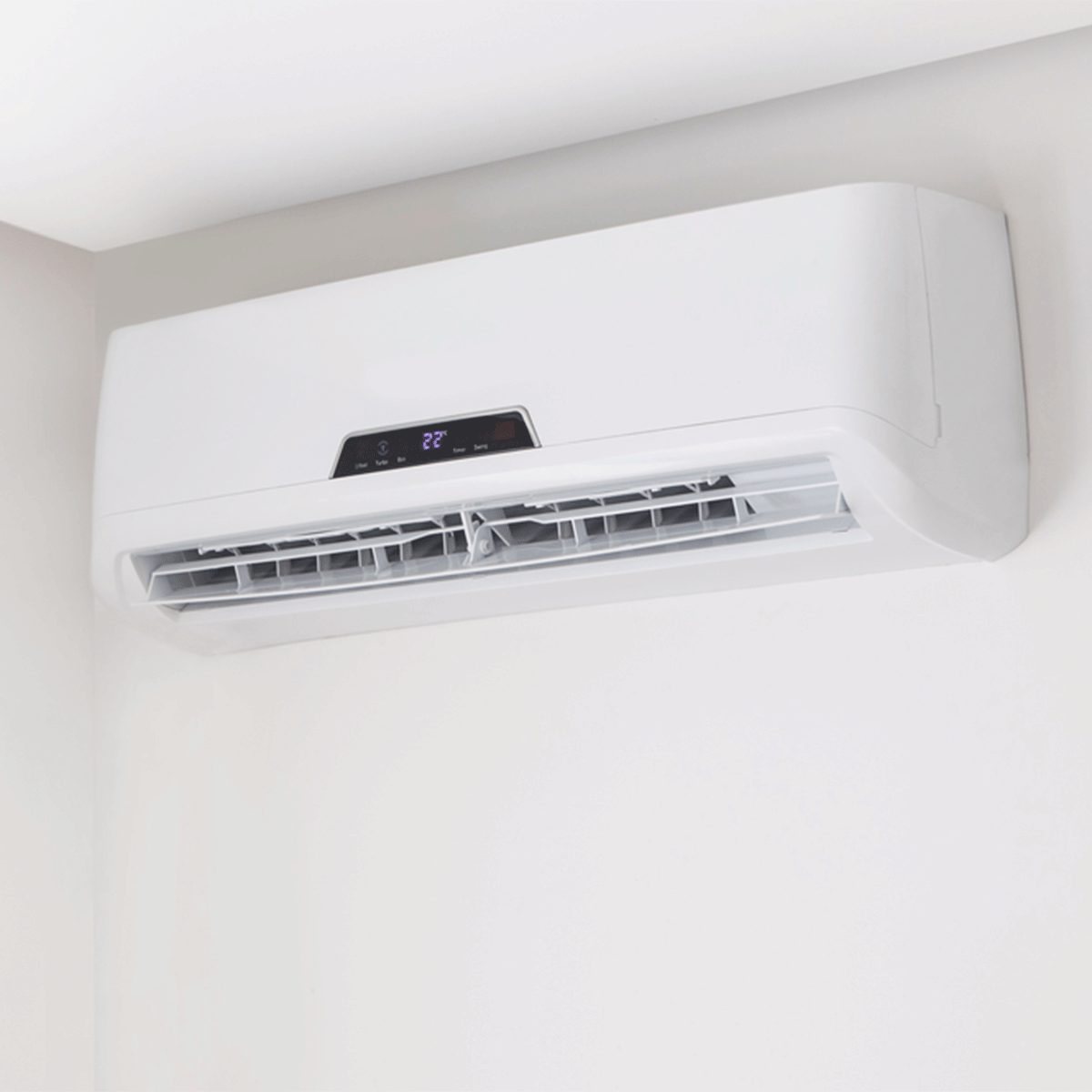 A white wall-mounted air conditioner displays a digital temperature reading of 22°C, positioned in a light-colored room.