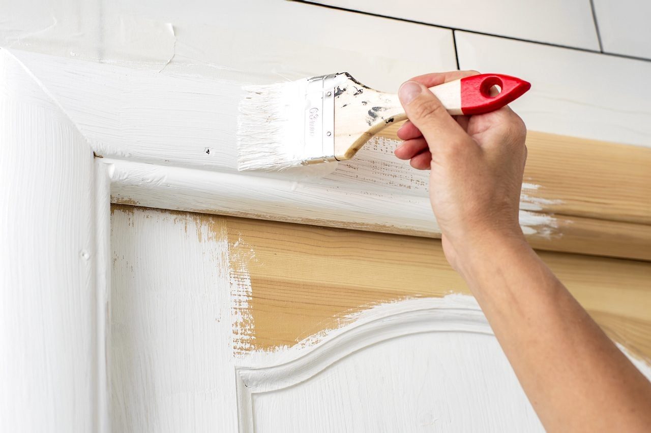 Hand with a brush paints a wooden door frame in white colo