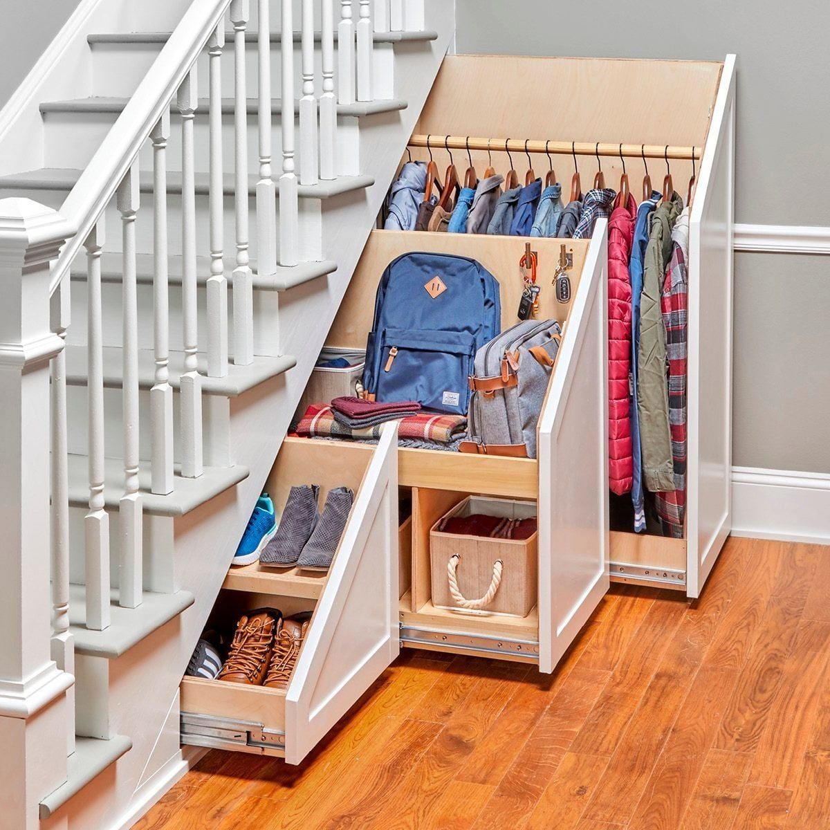 A wooden storage unit under a staircase holds clothing, shoes, and bags. It blends into the home’s interior with a polished floor and neutra