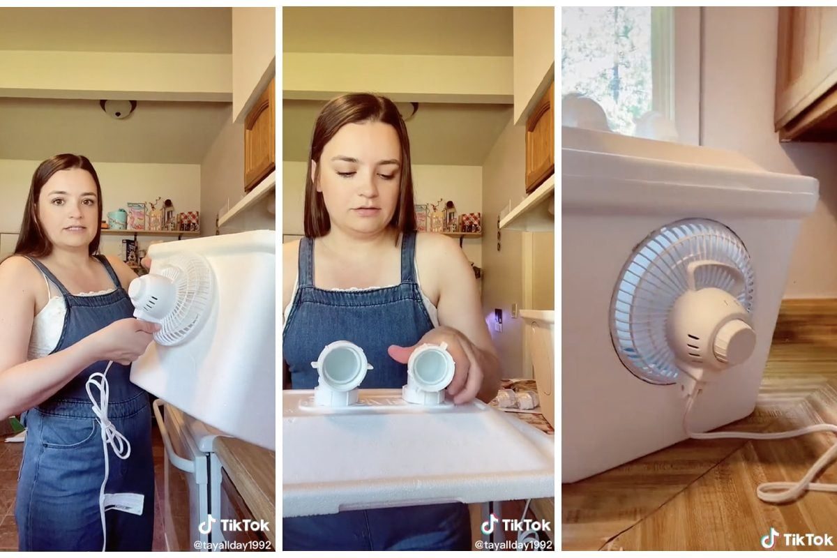A woman holds a portable fan connected to a cooler, preparing it while standing in a bright kitchen with shelves in the background.