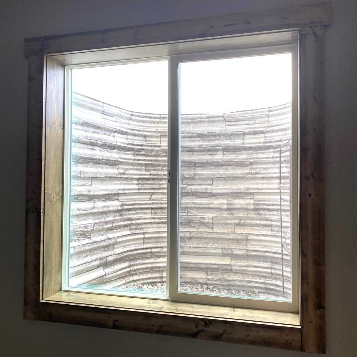 A large window reveals a curved stone wall outside, with a light-colored frame and gravel below, creating a serene, enclosed space.