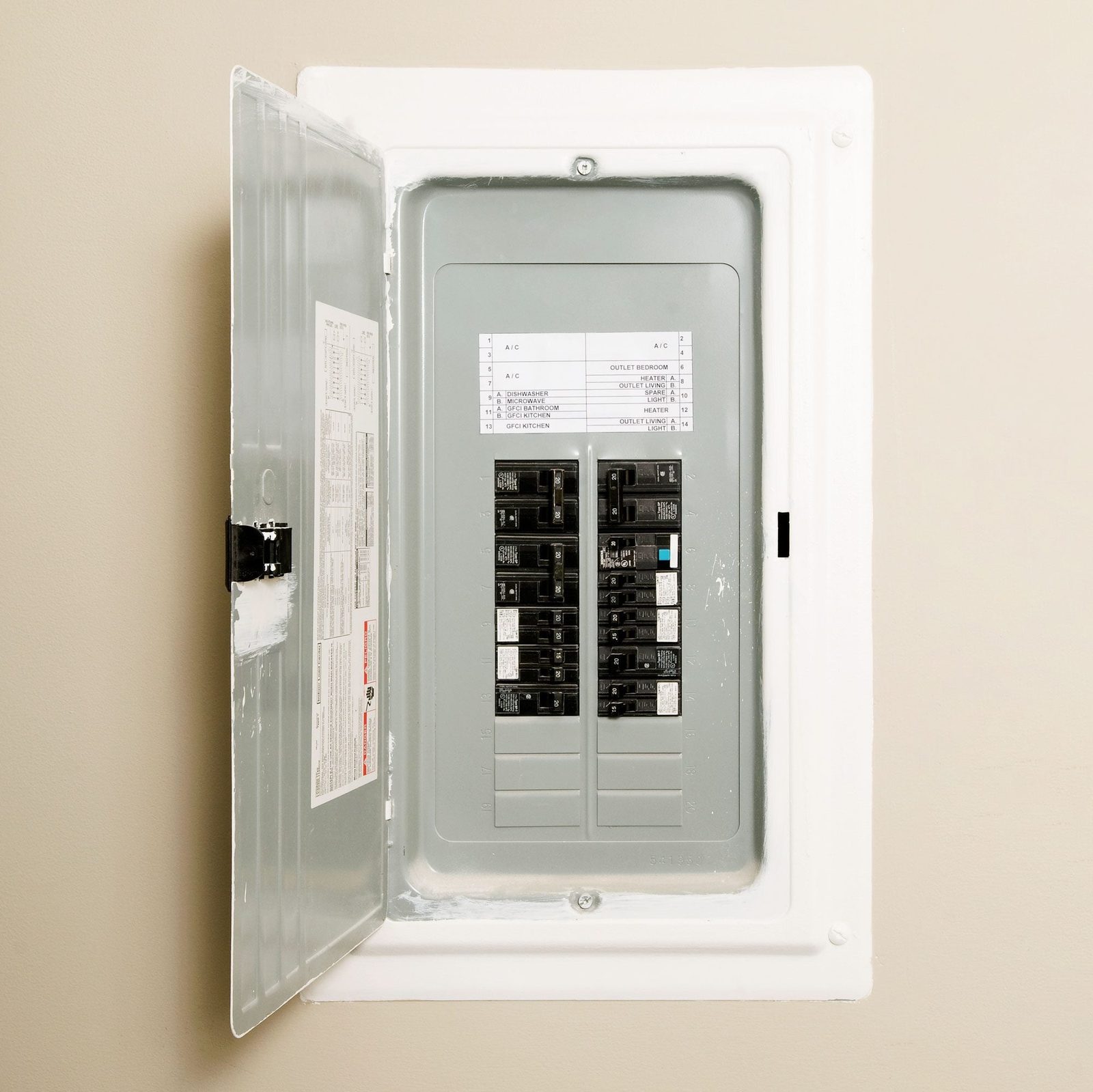 A gray electrical panel stands open against a beige wall, displaying various circuit breakers and a labeled chart for circuits and their fun