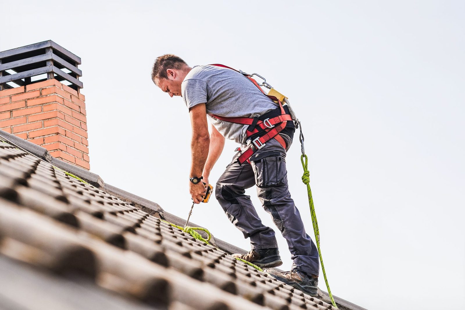 Electrician Wearing Safety Harness Tying Rope Standing On Roof