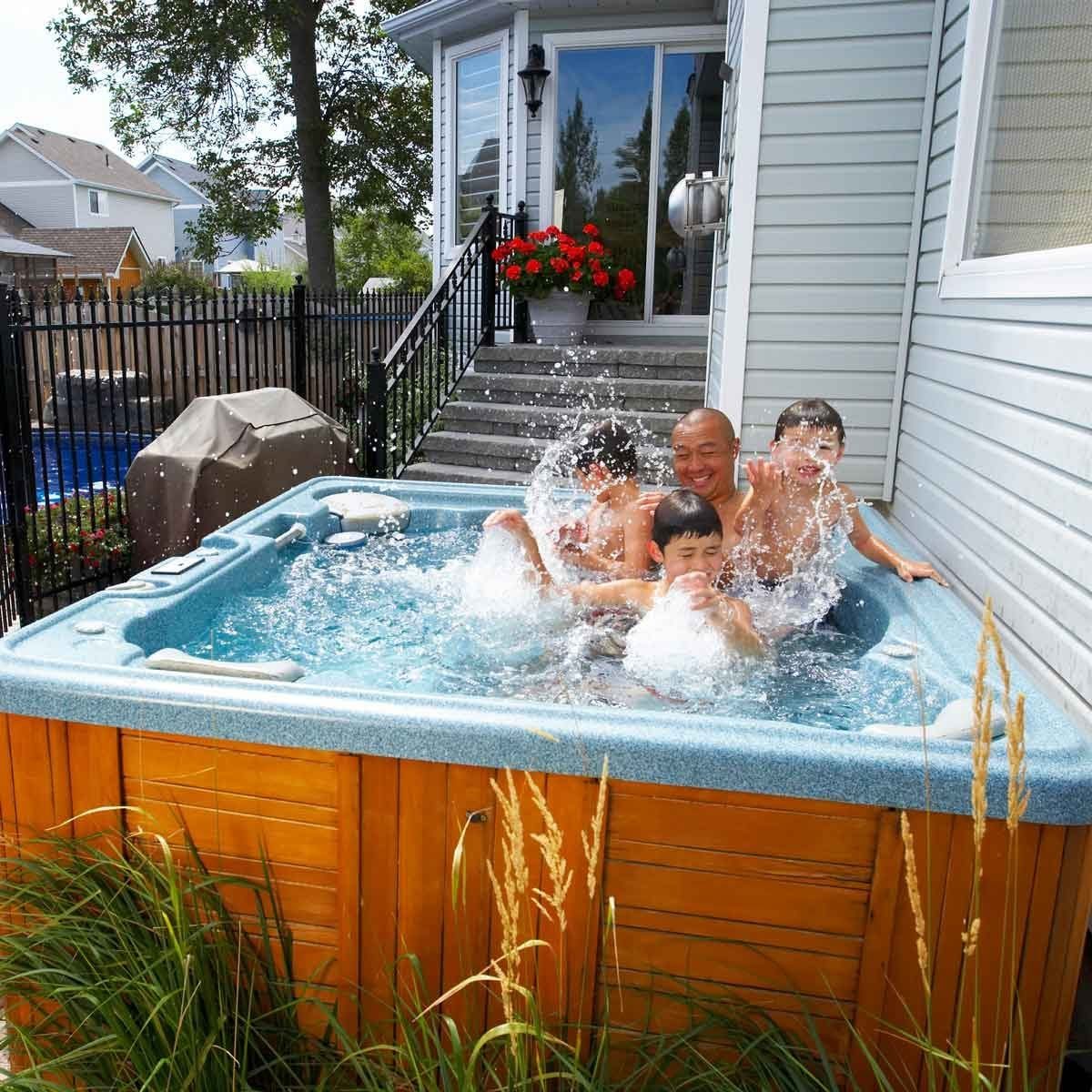 A family enjoys a splash-filled moment in a hot tub, surrounded by greenery and steps leading to a house, under a clear sky.