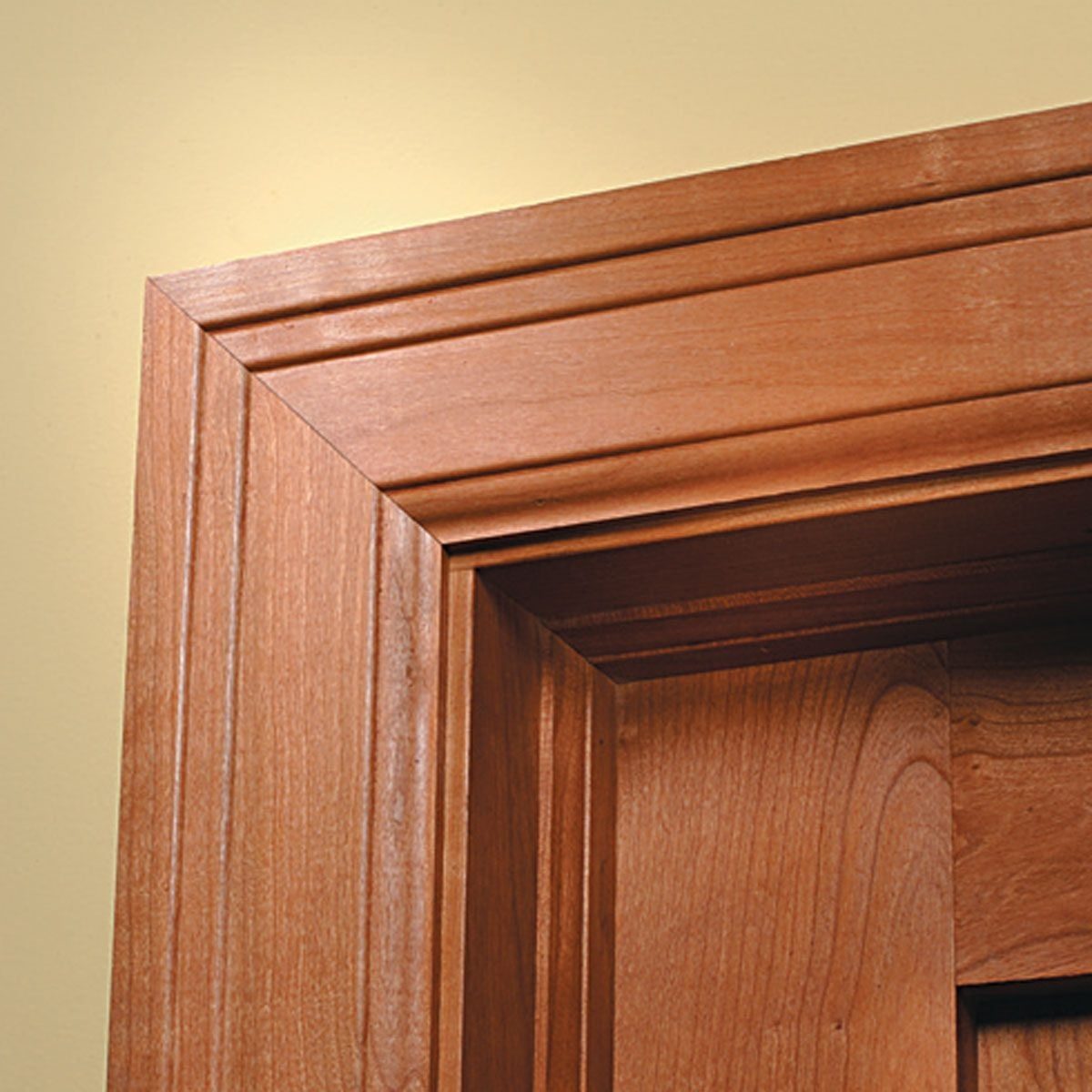 A wooden door frame, intricately designed with grooves, is positioned against a soft, light-colored wall, enhancing the craftsmanship of the