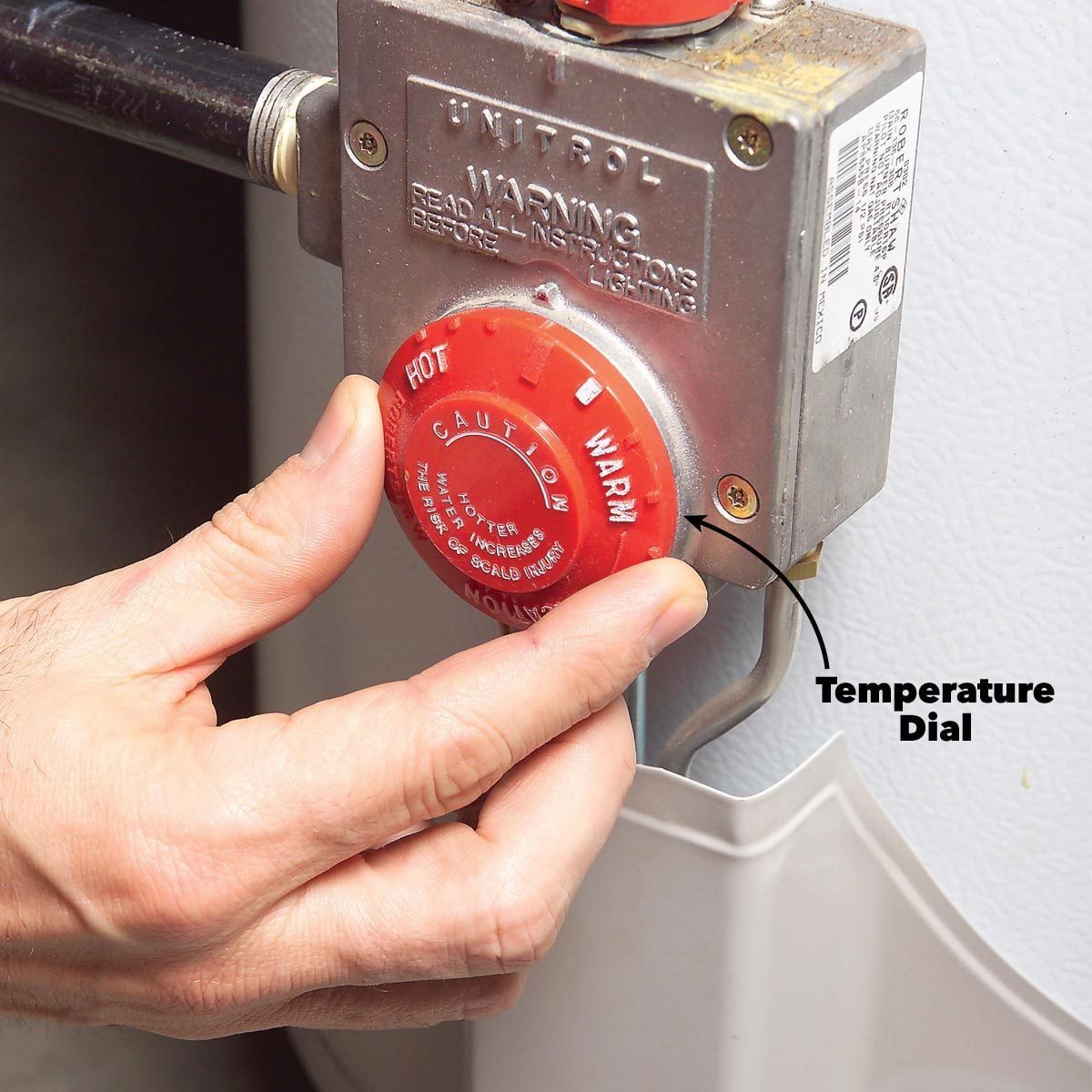 A hand adjusts a red temperature dial labeled "CAUTION" on a metal unit, set against a white background, indicating a heating or water syste