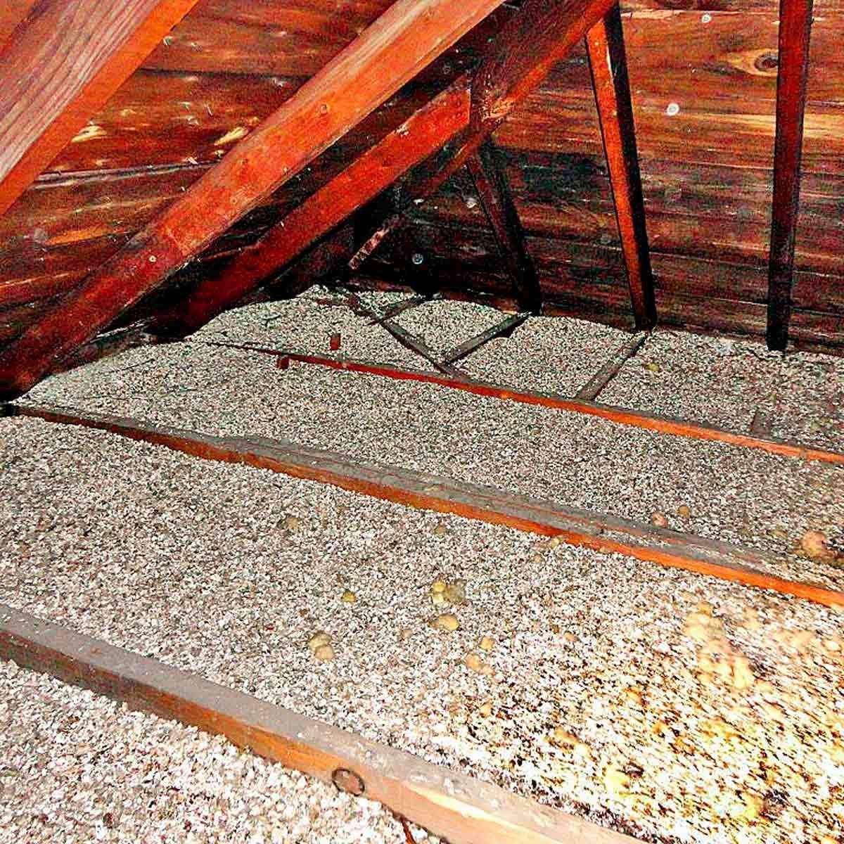 A wooden attic displays exposed beams, with a surface covered in gravel-like material, creating an uneven texture in a dimly lit environment