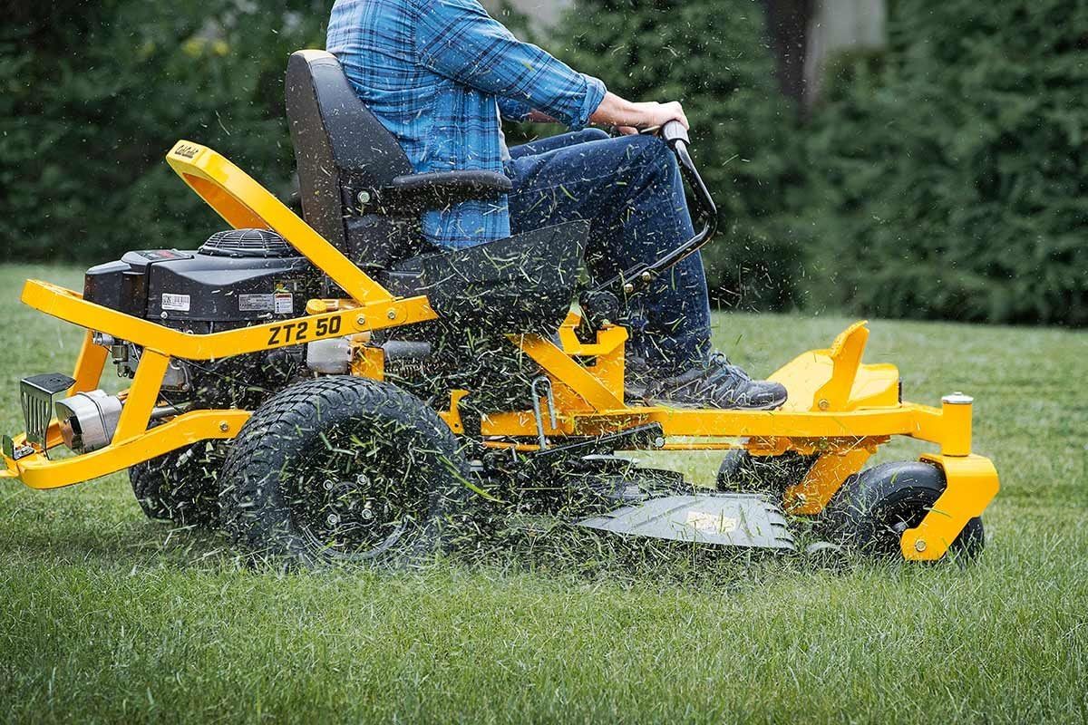 A riding lawn mower moves across a grassy area, cutting grass while ejecting clippings, with a person seated on it, focusing on lawn mainten