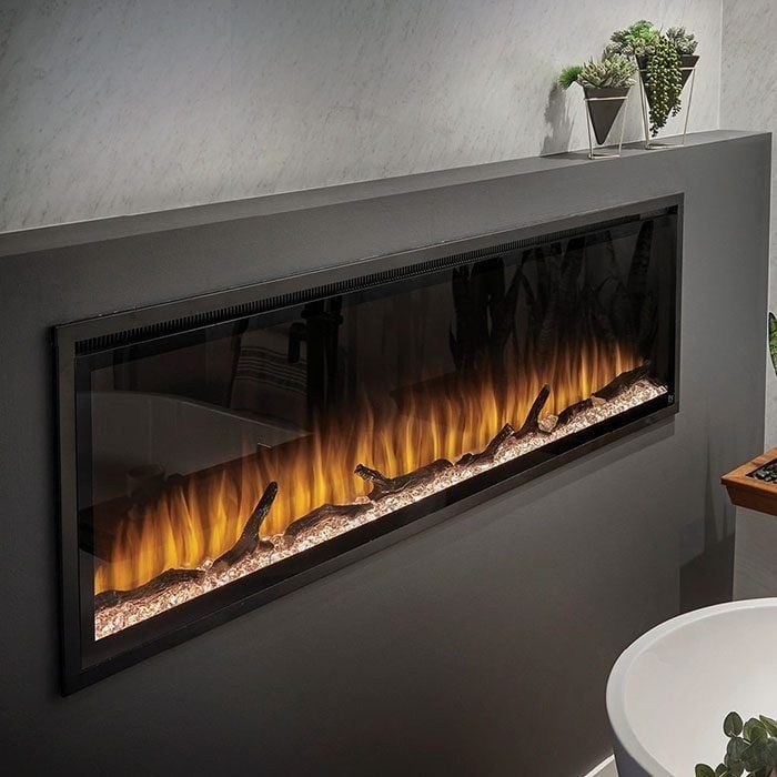 A modern wall-mounted electric fireplace emits a warm, glowing flame over pebbles, surrounded by a sleek, dark panel and plants in pots near