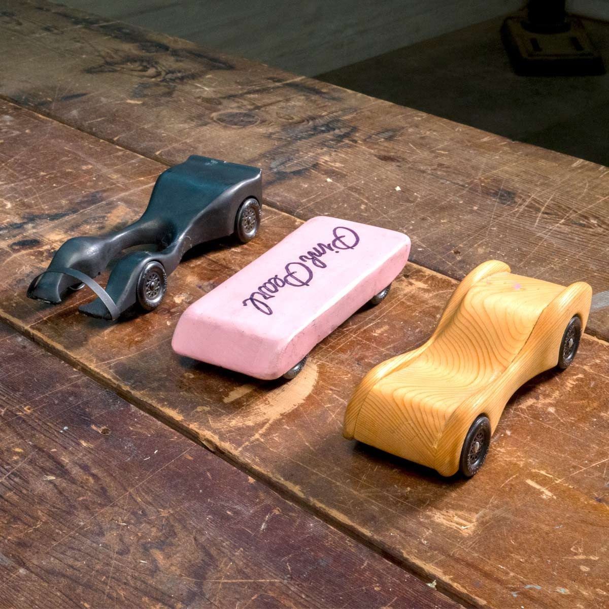 Three toy cars, each with distinct colors and shapes, sit on a wooden table, showcasing a playful and nostalgic atmosphere.