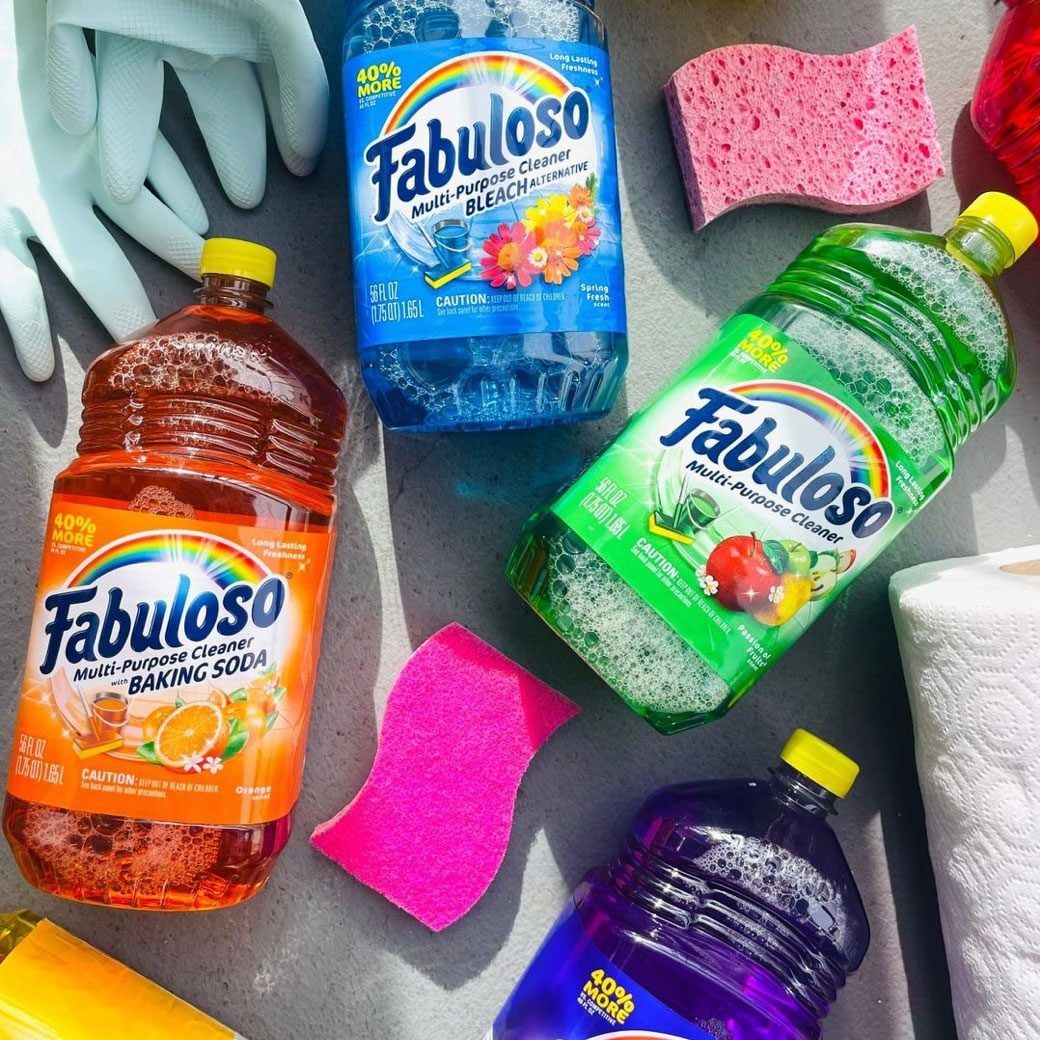 Bottles of Fabuloso cleaners in various colors are placed on a flat surface alongside sponges and paper towels, creating a vibrant cleaning