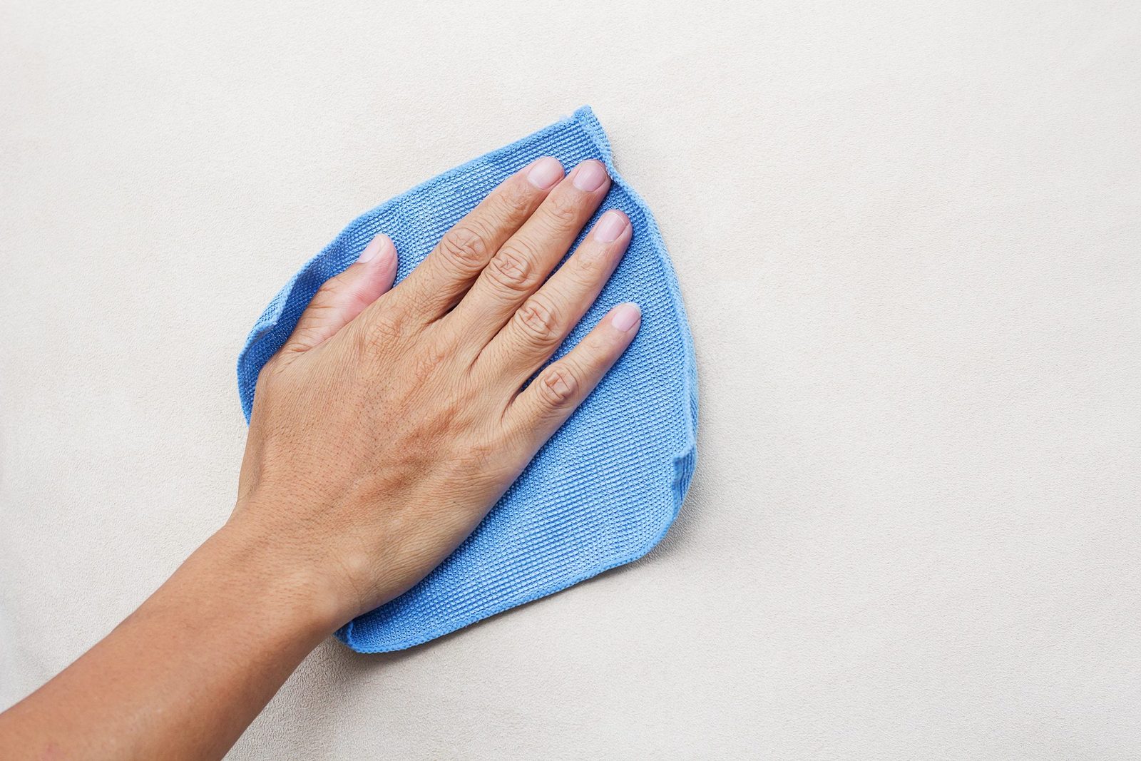 A hand wipes a smooth surface with a blue cloth, cleaning a light-colored area as part of a cleaning task.