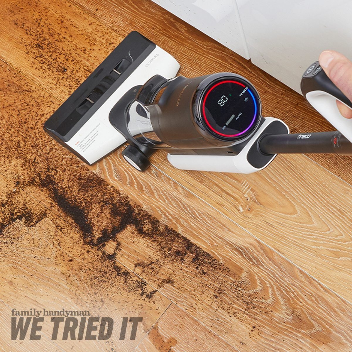 A vacuum cleaner is removing dirt from a wooden floor, while a digital display shows its operational status. Dark debris is visible on the f