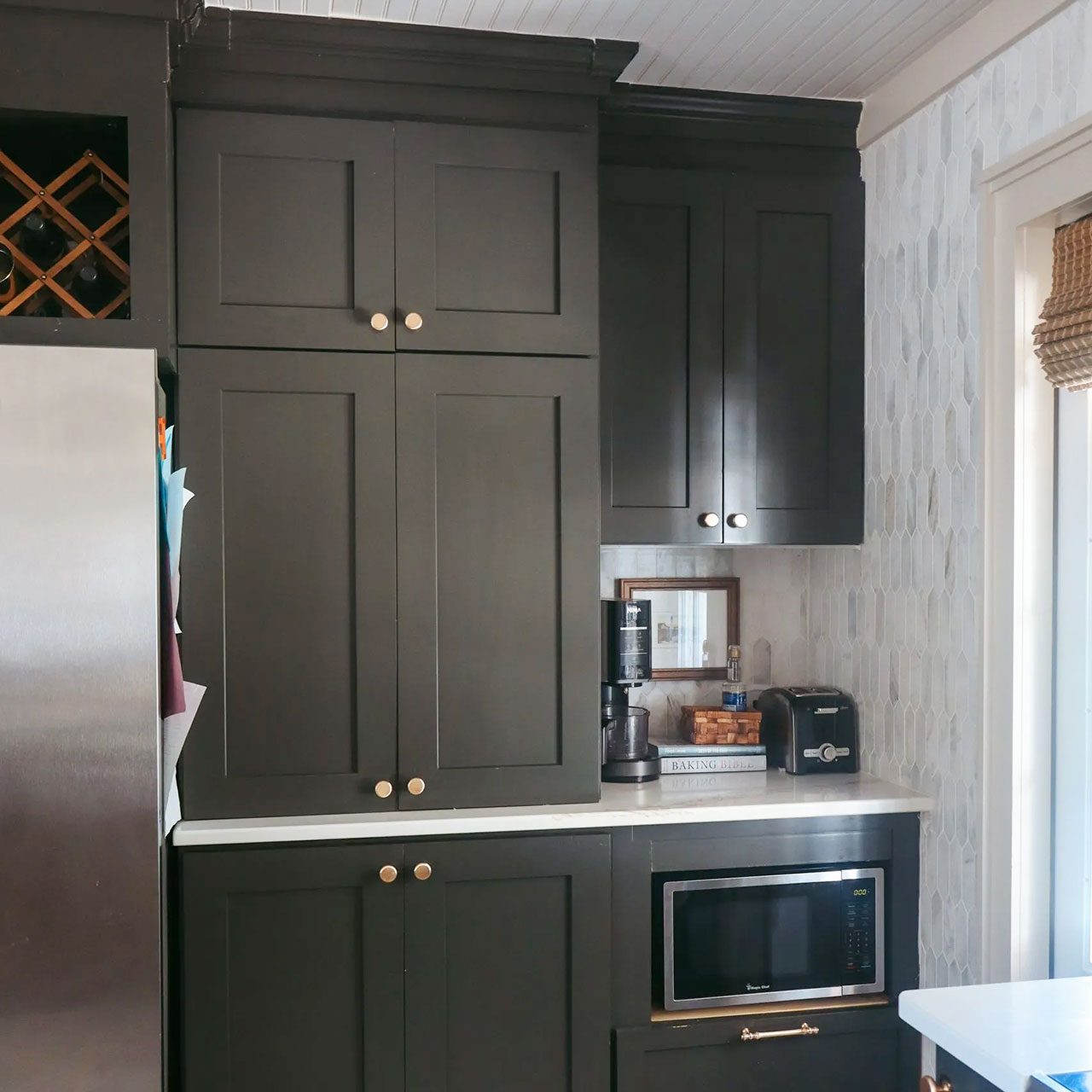 Modern kitchen with dark cabinets, white countertops, stainless steel appliances, a farmhouse sink, open shelving with dishes, and a window with natural light.