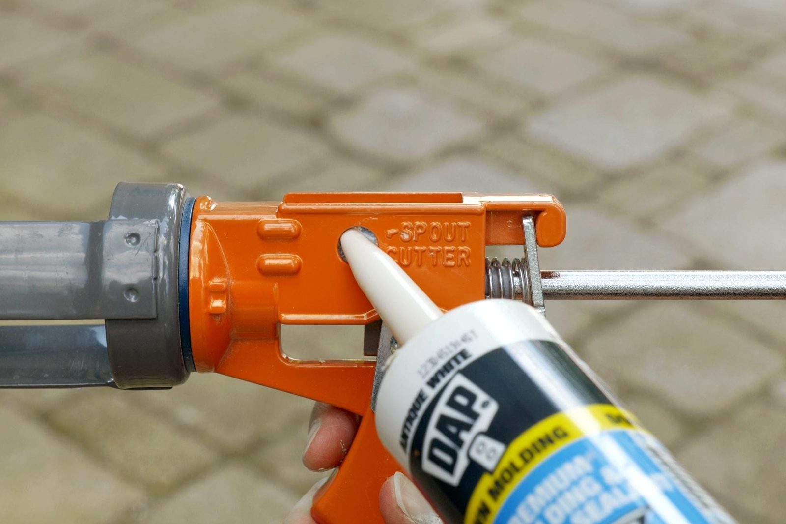 A tube of adhesive is being positioned into an orange caulking gun, with a stone surface in the background providing context for a DIY proje