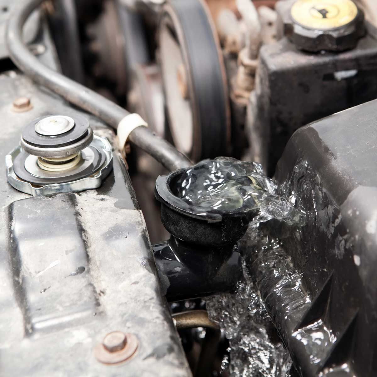 A radiator cap overflows, releasing coolant onto the engine compartment. Surrounding components include hoses and pulleys within a car's eng