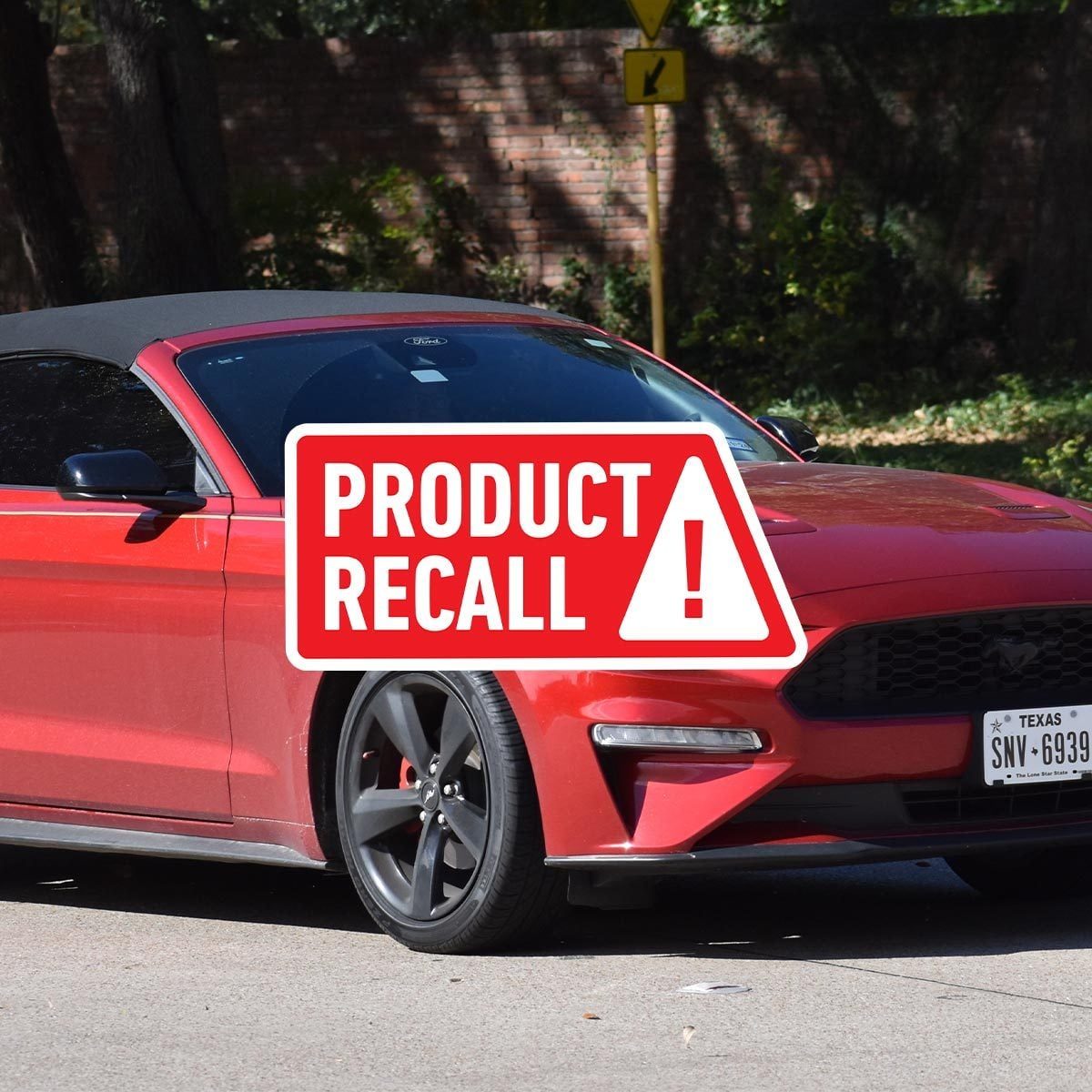 Red Ford Mustang driving on asphalt with a red "product recall" sticker on top