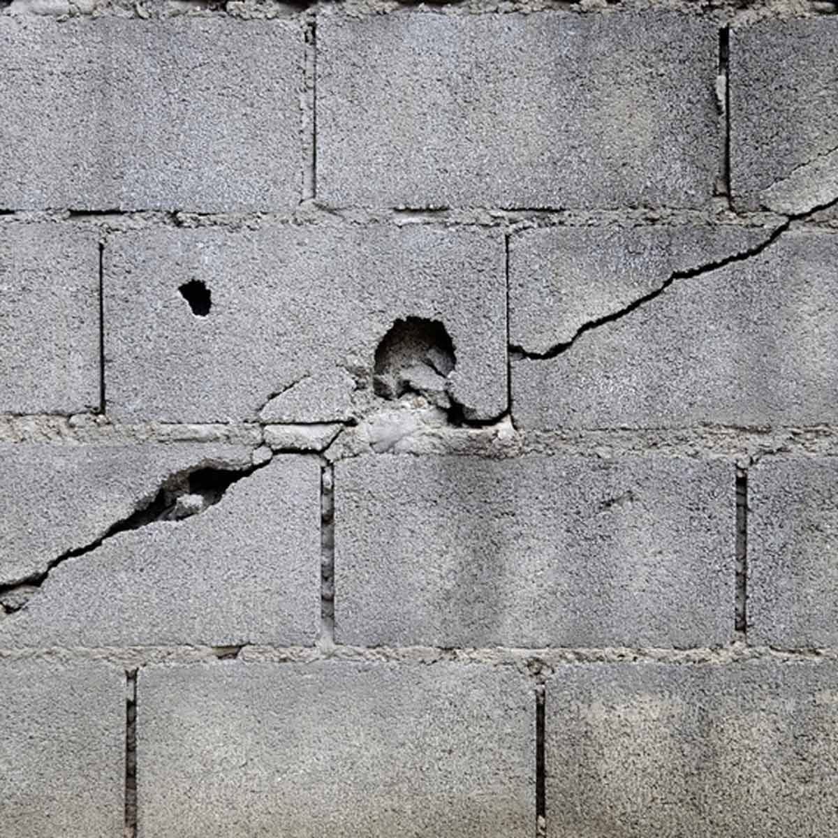 A gray concrete wall shows cracks and holes, indicating wear or damage. The texture appears rough, and the surface is unevenly lit.