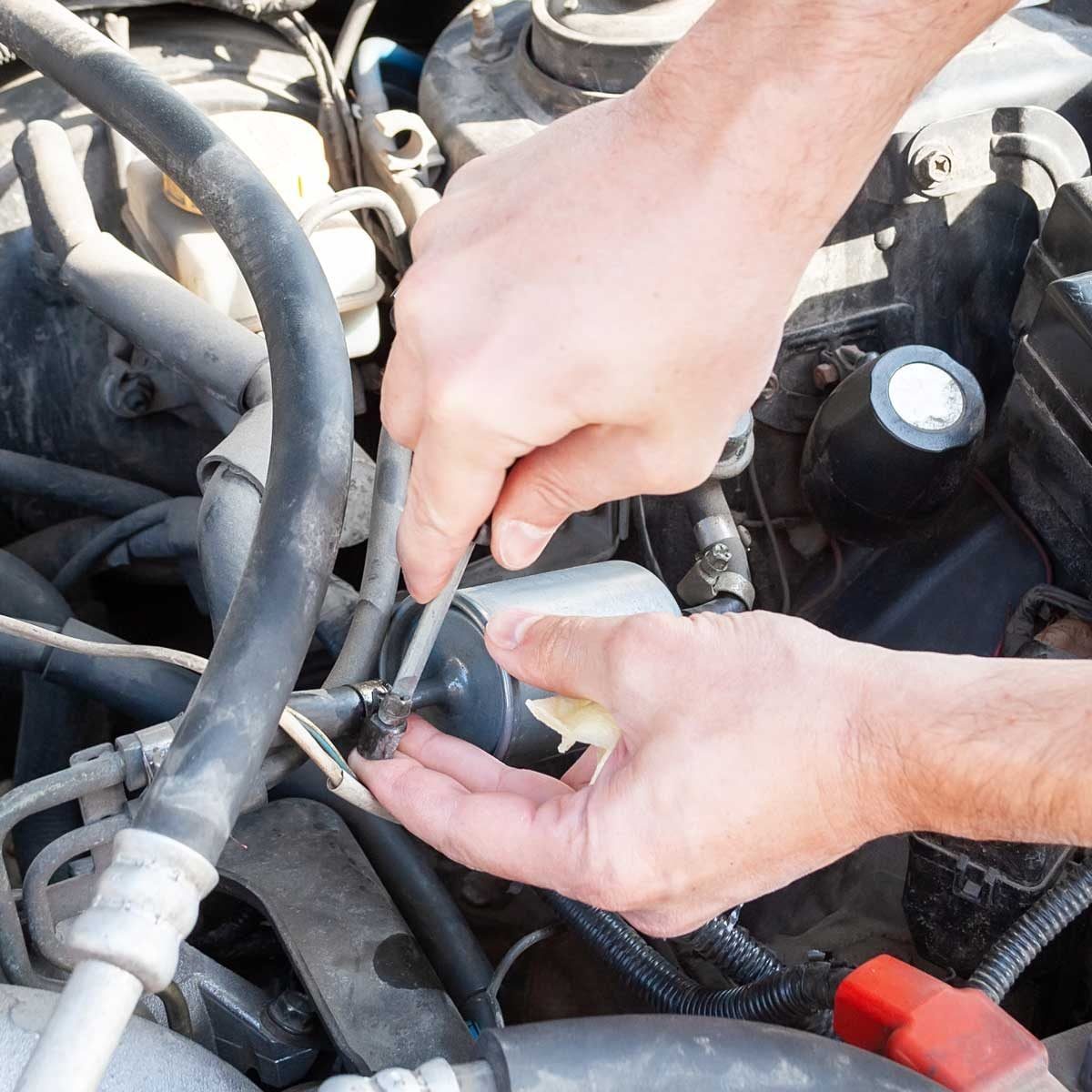 A person uses a wrench to tighten a connection on a metal component within a car engine, surrounded by various hoses and mechanical parts.