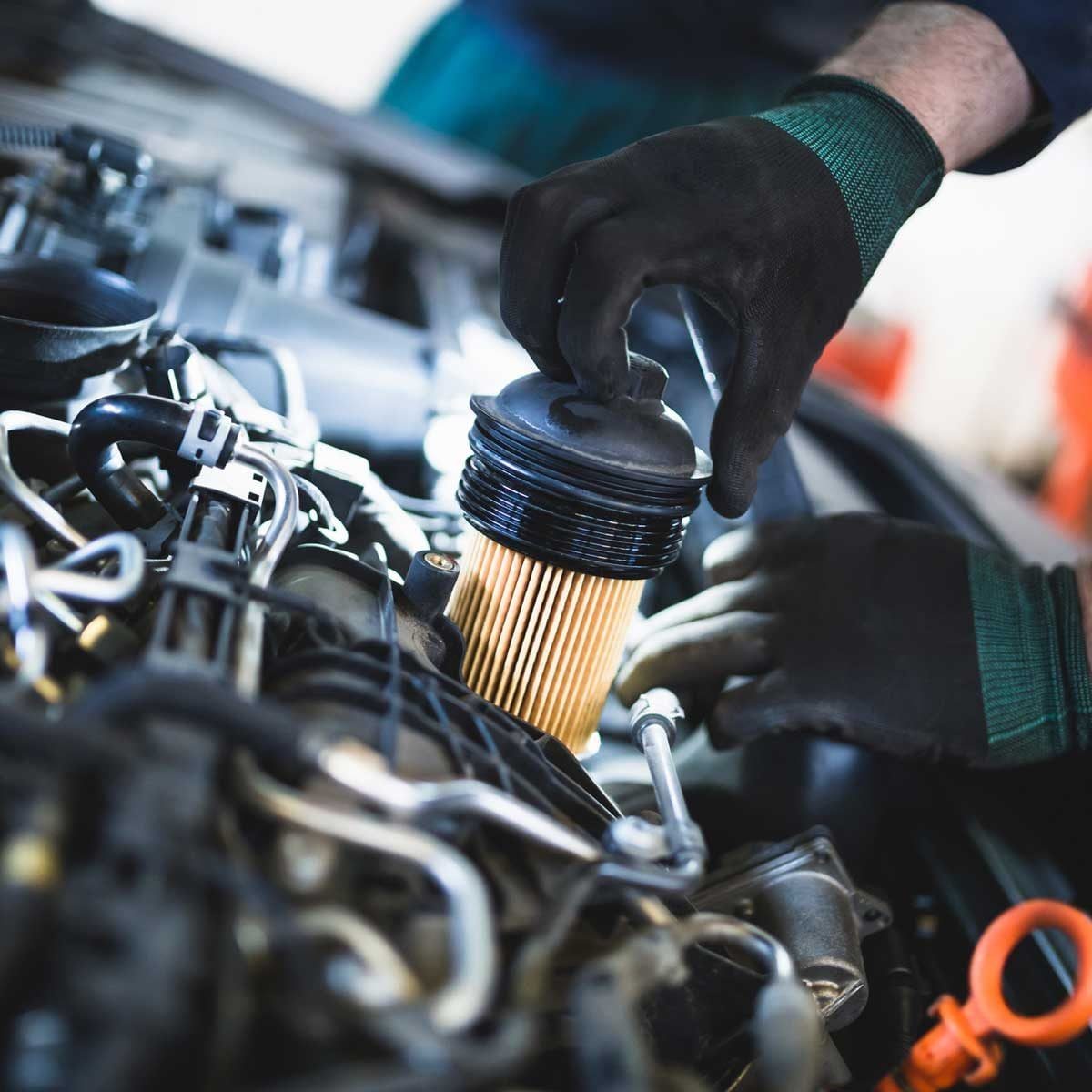 A mechanic installs an oil filter in a car engine, surrounded by various engine components and tools, indicating automotive maintenance in a