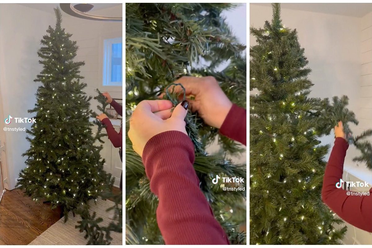 A person is adding decorative lights to an artificial Christmas tree in a well-lit room with wooden flooring and a white wall.