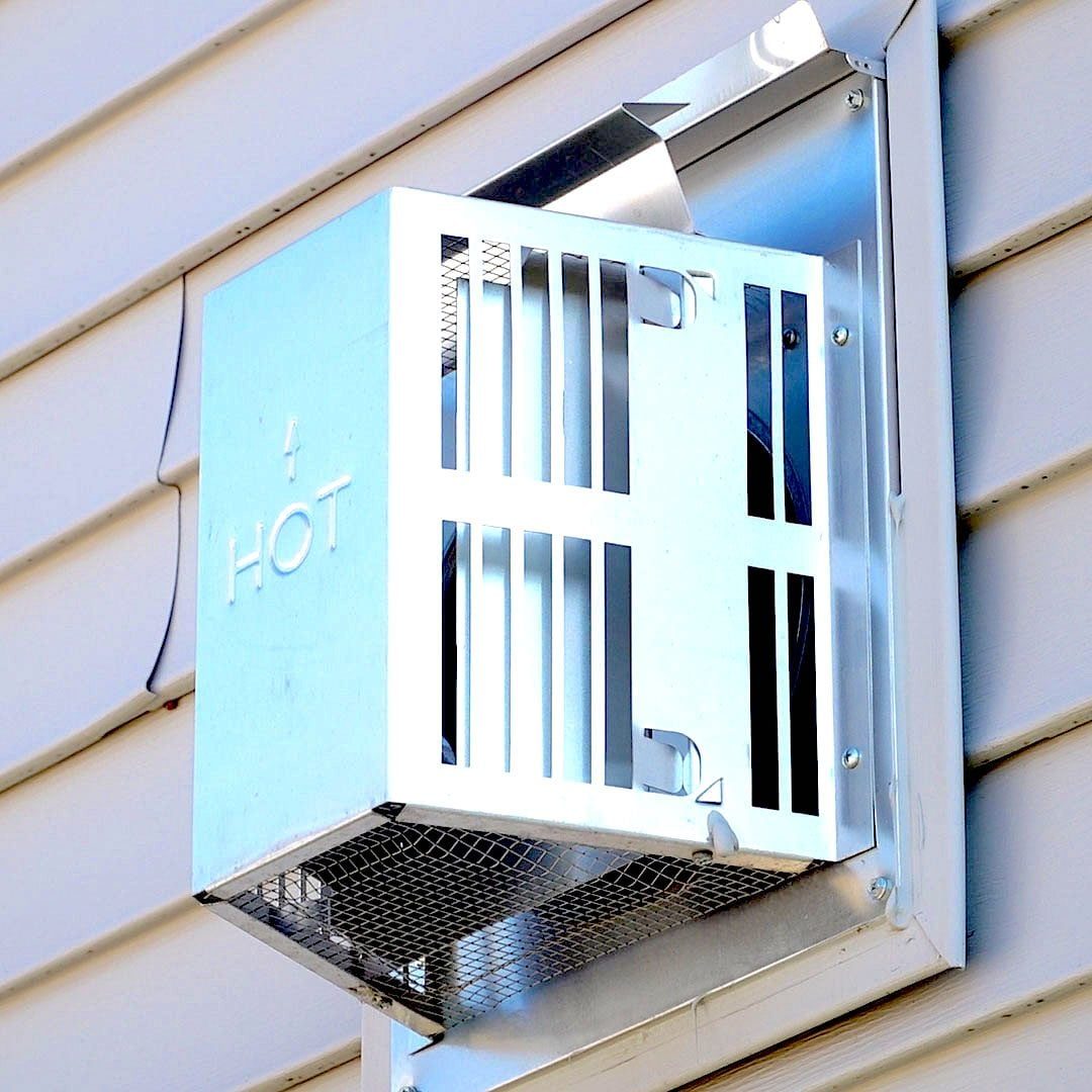 A metal vent is mounted on a wall, expelling hot air while metal slats and a mesh cover provide ventilation, against a light-colored siding