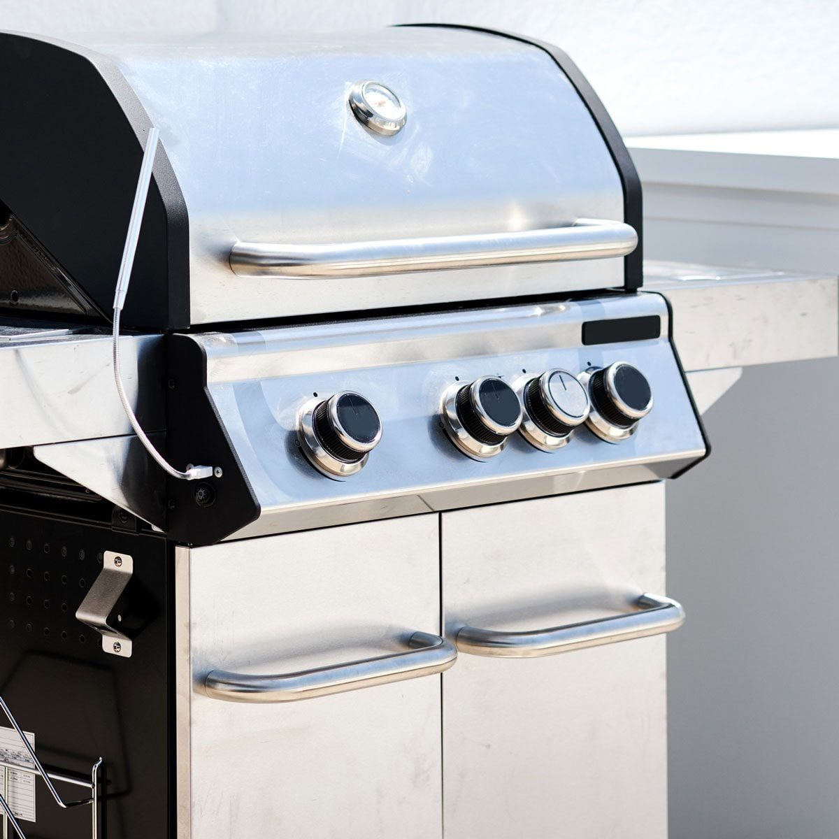 A stainless steel gas grill sits on a countertop, featuring four control knobs and a silver lid, showcasing a clean, modern outdoor cooking
