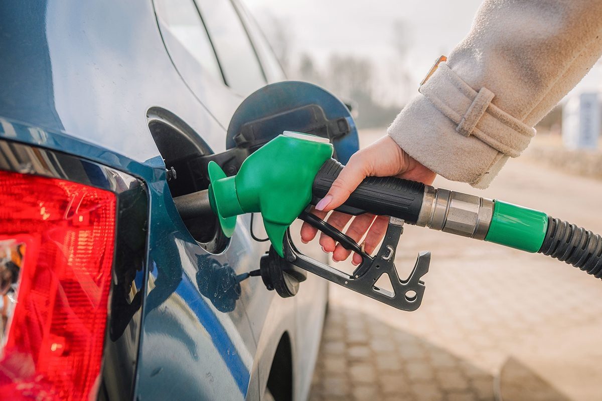Hand holding green fuel nozzle while refueling a blue car at a gas station