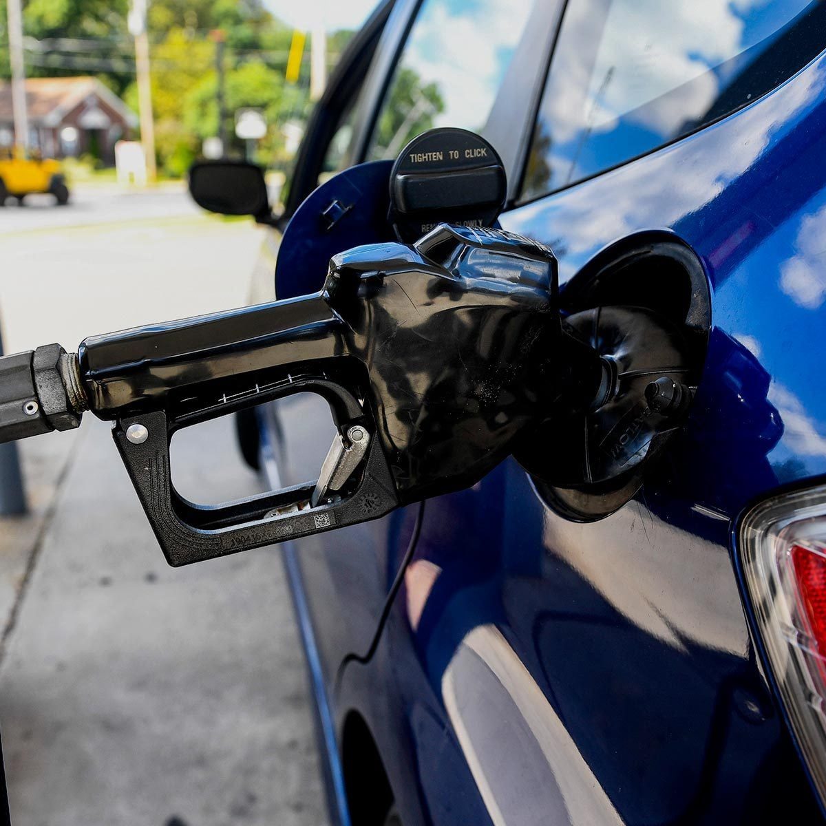 Black gas pump sits in a blue car's gas tank opening at a gas station
