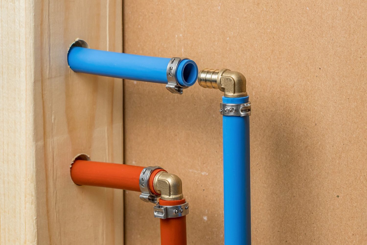 Two colored pipes, one blue and one red, connect at a brass fitting, mounted on a wooden surface, showcasing plumbing installation.